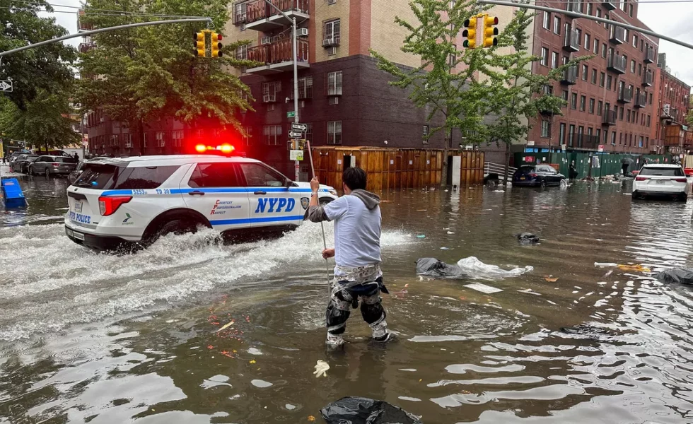 man in a deeply flooded NYC street with an NYPD car driving by