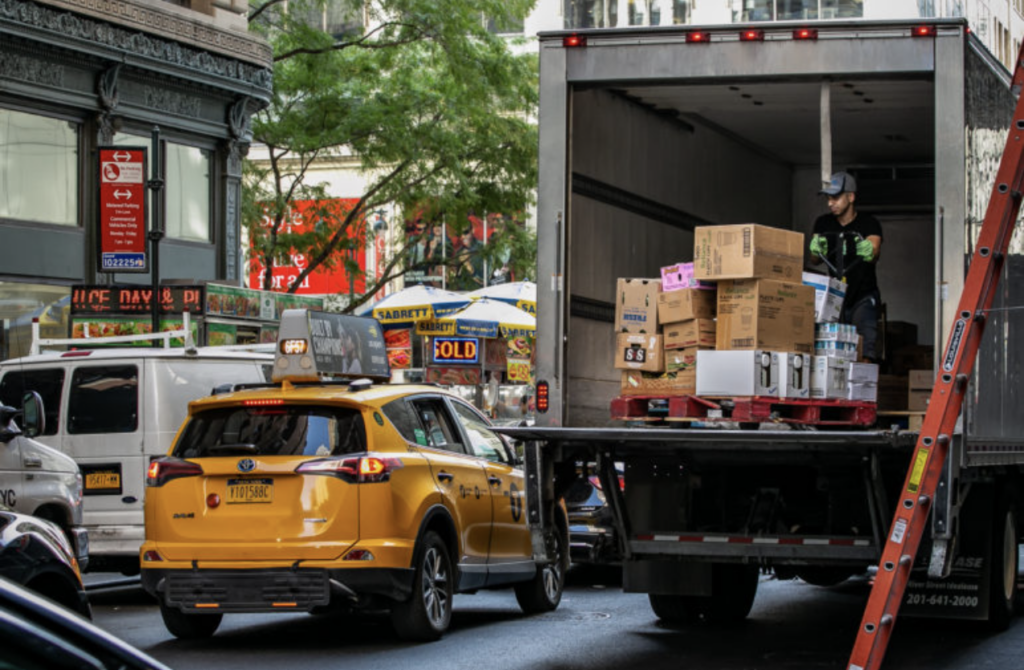 NYC street with a cab and boxes being moved out of a truck