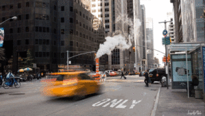 gif of a NYC street with a taxi driving and steam coming off of a construction zone